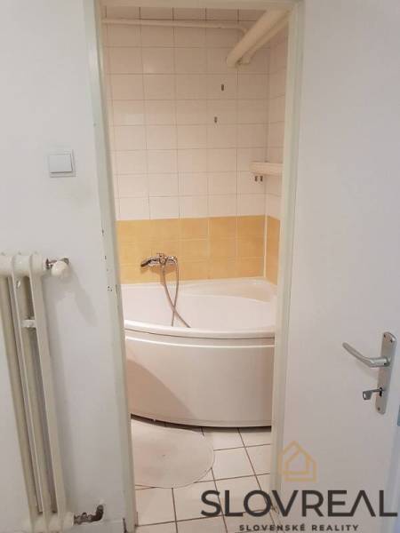 PREDAJ 2 IZBOVÝ BYT HANDLOVÁ  - Kúpeľňa s rohovou vaňou v 2-izbovom byte, vidieť radiátor a dvere.