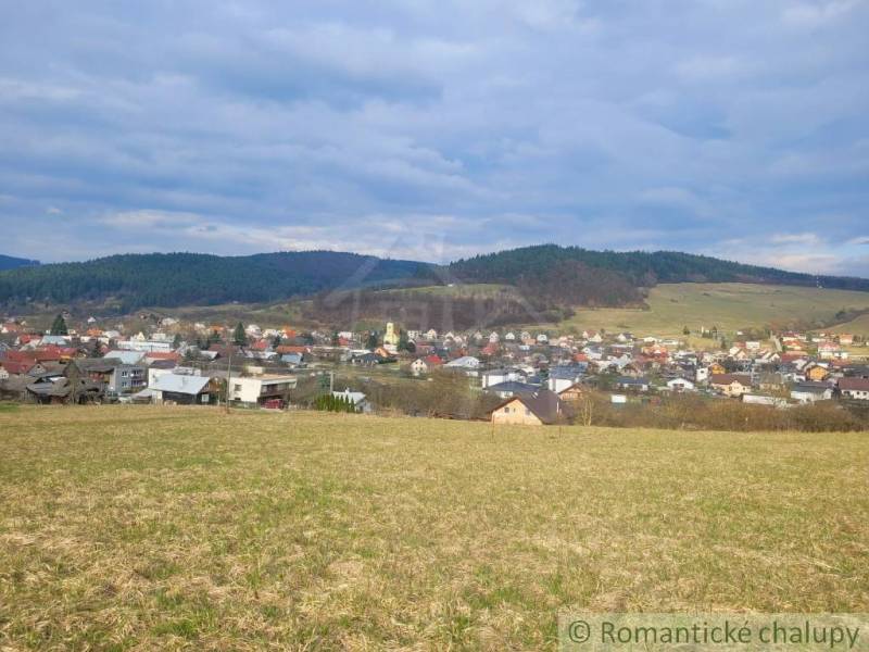 Stavebný pozemok s krásnym výhľadom nad obcou Jasenica pri Považskej B - Panoráma Jasenice so záhradami, obklopená políami a lesmi pod modrou oblohou.