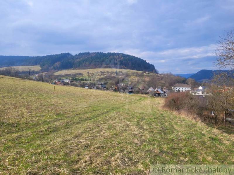 Stavebný pozemok s krásnym výhľadom nad obcou Jasenica pri Považskej B - Krajina v Záhradách Jasenice: Zeleň, kopce a domčeky pod oblačným nebom.