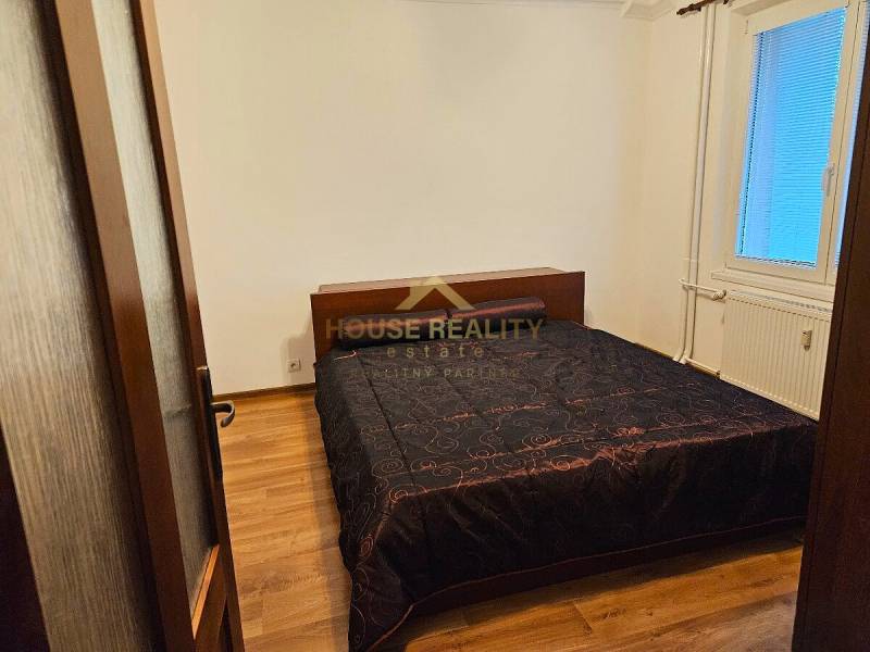 Prenájom pekný 3 izbový byt, Haburská ulica, Bratislava II. Ružinov - Spálňa v 3-izbovom byte s podlahou s dreveným dekorom a tmavým lôžkovinovým prehozom.