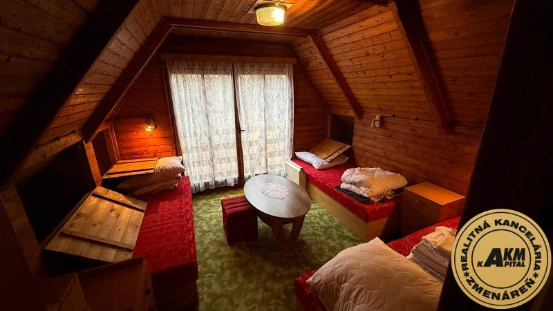 PRIPRAVUJEME Rekreačná chata - Zvolen - Kováčová na Predaj - Interiér chaty s dreveným obložením, tromi posteľami a okrúhlym stolíkom.