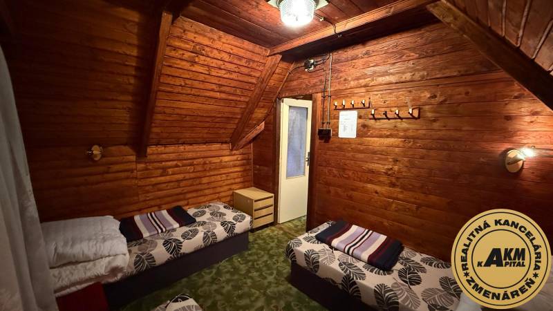 PRIPRAVUJEME Rekreačná chata - Zvolen - Kováčová na Predaj - Interiér chaty s dreveným obložením, posteľami a lustrom, útulné prostredie na relaxáciu.
