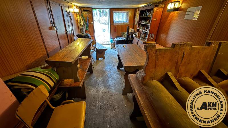 PRIPRAVUJEME Rekreačná chata - Zvolen - Kováčová na Predaj - Interiér chaty s drevenými stolmi a lavicami, výhľad na záhradu.