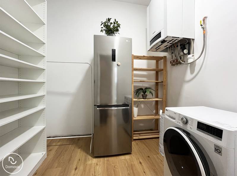 Exkluzívne | Na predaj výnimočný 2i byt pri Trnavskom mýte  - Chladnička a práčka v 2-izbovom byte na ulici Vajnorská, doplnené policami a rastlinami.