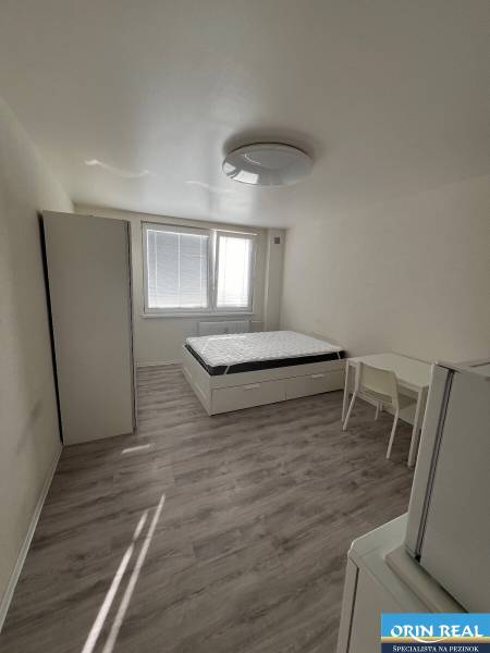 ZREKONŠTRUOVANÁ ZARIADENÁ GARSÓNKA - Garsónka s posteľou, skriňou, stolom a podlahou s dreveným dekorom.