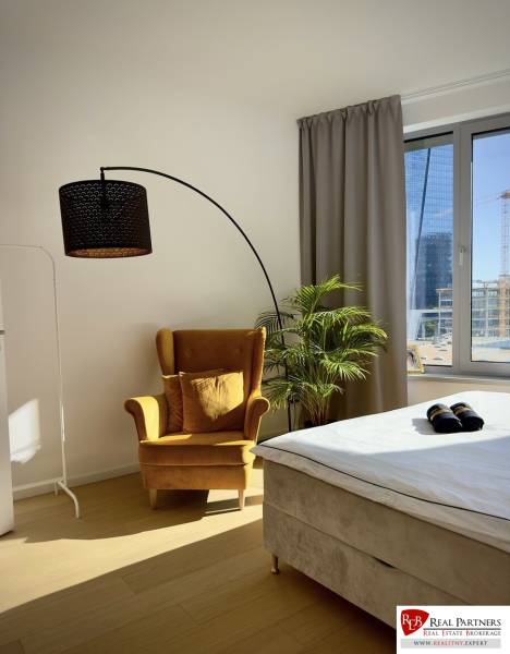 Prenájom 3-izbový byt s loggiou, SKY PARK, Bratislava - Izba v 3-izbovom byte s kreslom, podlahou s dreveným dekorom a veľkým oknom.