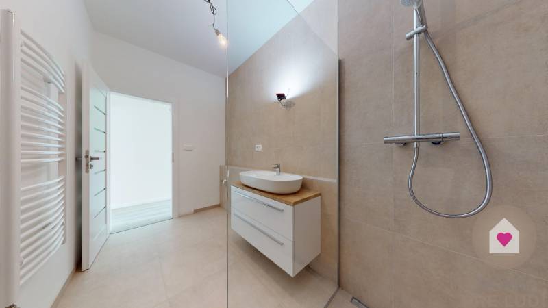 3i. BYT S VLASTNÝM TEP. ČERPADLOM + KLIMATIZÁCIA A EXTERIÉROVÉ ŽALÚZIE - Kúpeľňa v 3-izbovom byte s umývadlom, sprchou a otvorenými dverami.