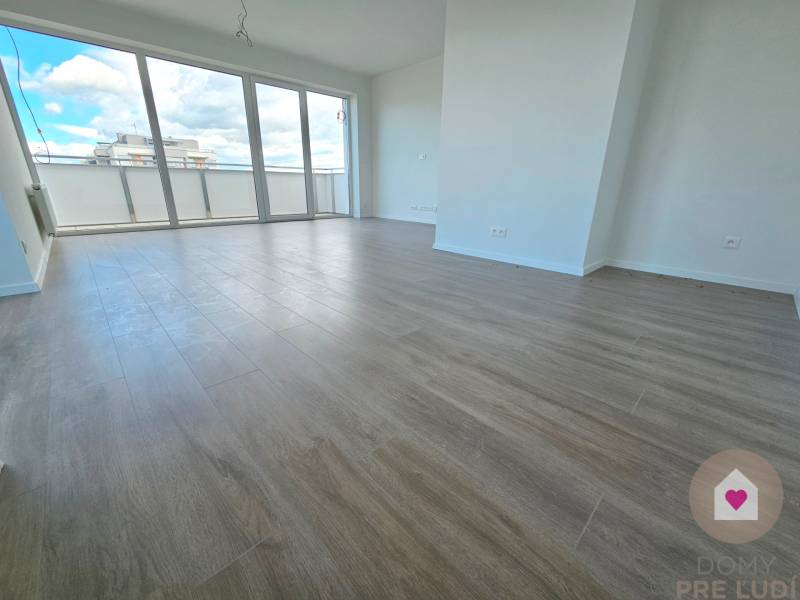 3i. BYT S VLASTNÝM TEP. ČERPADLOM + KLIMATIZÁCIA A EXTERIÉROVÉ ŽALÚZIE - Priestranná obývacia izba s drevenou podlahou a veľkými oknami v 3-izbovom byte.