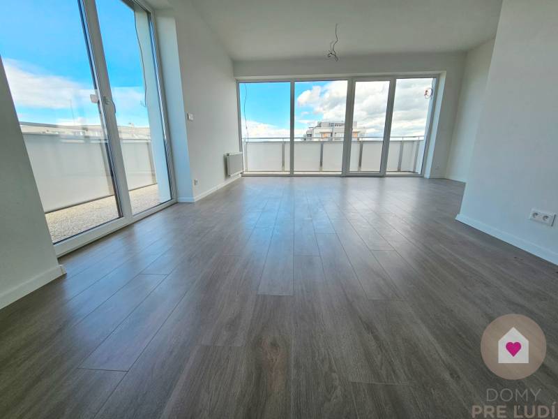 3i. BYT S VLASTNÝM TEP. ČERPADLOM + KLIMATIZÁCIA A EXTERIÉROVÉ ŽALÚZIE - Priestranná obývačka s veľkými oknami a drevenou podlahou v 3-izbovom byte.