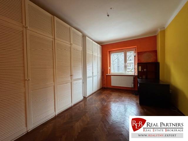 Predaj 3 izbový byt, 86 m2, Francisciho ul, Staré mesto, BAI . - Izba s oranžovou stenou, veľkou skriňou a podlahou s dreveným dekorom v 3-izbovom byte.