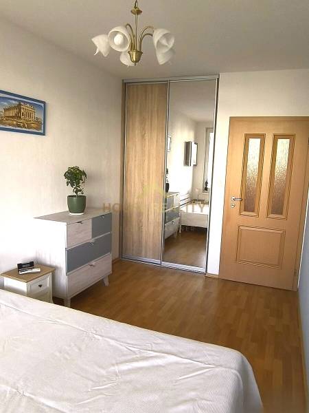 Novostavba s parkovaním 2 izbový byt, Jégeho ulica, BA II. Ružinov - Spálňa so vstavanou skriňou, drevený dekor podlahy, skrinka, posteľ, luster, rastlina.