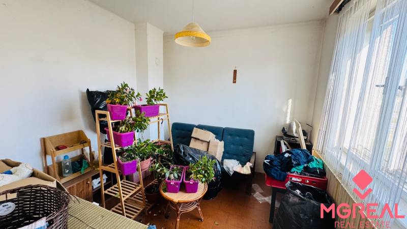 Na predaj 3 i RD v Partizánskom – Veľké Bielice, pozemok 1149 m2 - Izba v rodinnom dome s rastlinami, sedačkou a stolíkom pred veľkým oknom.