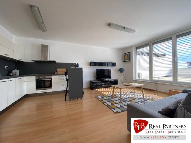 Prenájom 2 izbový 78 m2 + 30 m2 terasa,novostavba Koliba,zariadený - Obývacia izba 2-izbového bytu s podlahou s dreveným dekorom, kuchyňou a oknami.