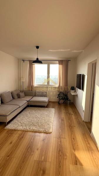 Prenájom pekný 3 izbový byt Jankolova ulica, Bratislava V. Petržalka - Obývacia izba v 3-izbovom byte s podlahou s dreveným dekorom a svetlou sedačkou.