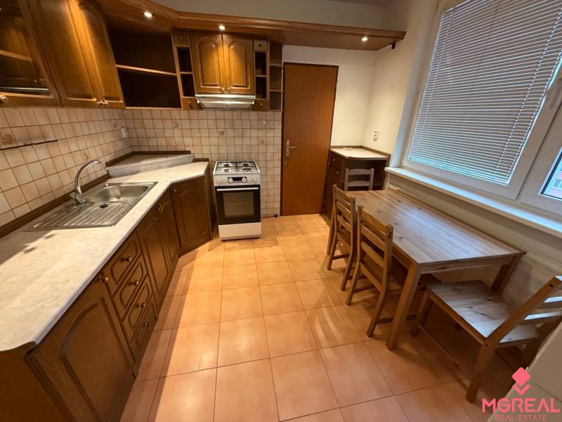 2 izbový byt s balkónom Topoľčany  - Kuchyňa 3-izbového bytu s dreveným dekorom skriniek a jedálenským sedením.