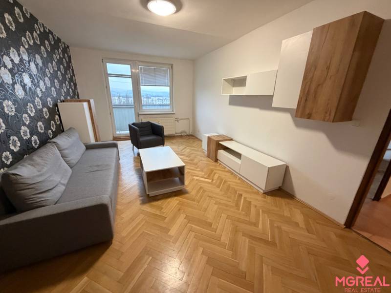 2 izbový byt s balkónom Topoľčany  - Obývacia izba v 3-izbovom byte so sivou sedacou súpravou a kvetinová tapeta na stene.