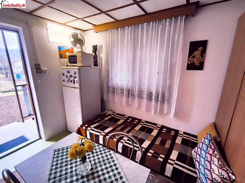 ‼️BRODZANY - ZÁHRADA S MUROVANOU CHATKOU NA PREDAJ, okr. PARTIZÁNSKE‼️ - Interiér chaty s chladničkou, gaučom, stolom a výhľadom do záhrady.