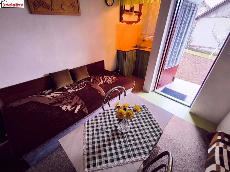 ‼️BRODZANY - ZÁHRADA S MUROVANOU CHATKOU NA PREDAJ, okr. PARTIZÁNSKE‼️ - Interiér chaty s pohovkou, jedálenským stolom a otvorenými dverami do záhrady.