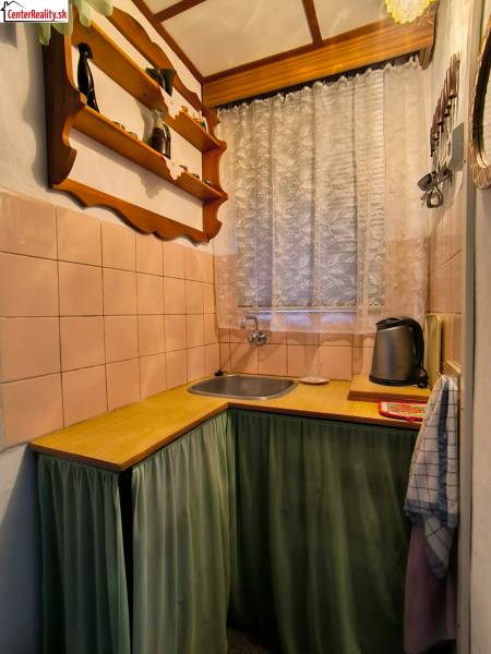 ‼️BRODZANY - ZÁHRADA S MUROVANOU CHATKOU NA PREDAJ, okr. PARTIZÁNSKE‼️ - Kuchynka v chate s dreveným dekorom, poličkou a závesom pri okne.