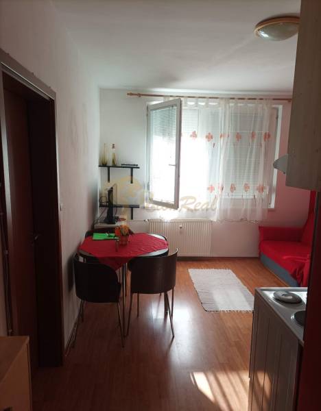 1-izb. byt, Pezinok - Sever, ul. Suvorovova - Obývacia časť 1-izbového bytu s podlahou s dreveným dekorom, stolom a stoličkami.