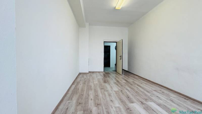 Kancelária s výhľadom na centrum Michaloviec. 16 m2 - Kancelárie s bielymi stenami a podlahou s dreveným dekorom, otvorené dvere.