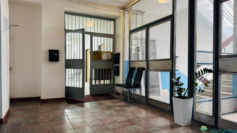 Kancelária s výhľadom na centrum Michaloviec. 16 m2 - Vstup do kancelárie s presklenými dverami, rastlinou a sedením.