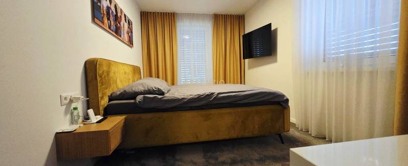 - KRÁTKODOBÝ PRENÁJOM - RODINNÝ DOM - 105 m2 - ROVINKA - Spálňa v rodinnom dome s posteľou, nočný stolík, TV a závesmi.