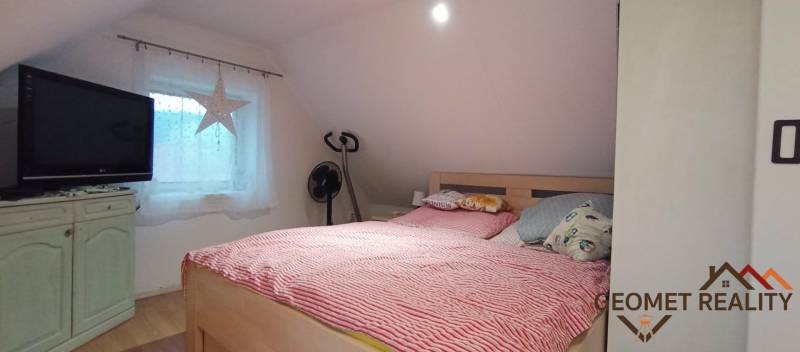 Útulný domček s dušou a moderným komfortom – Divín - Spálňa v podkroví rodinného domu s posteľou, televízorom a podlahou s dreveným dekorom.