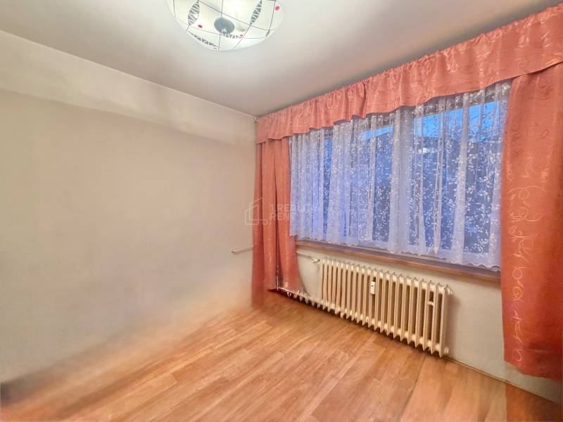 Predaj pôvodného 3+1 bytu v žiadanej lokalite v Čadci (MO) - Izba v 3-izbovom byte s podlahou s dreveným dekorom a závesmi.