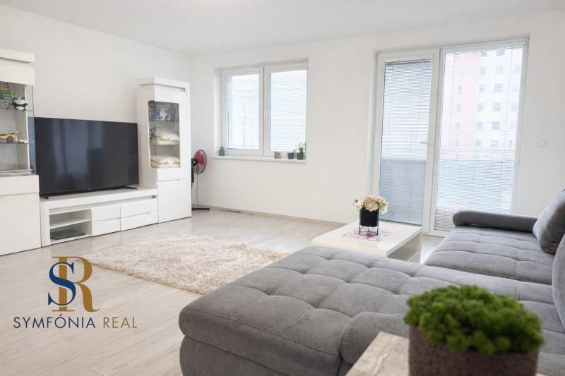 2-izbový byt novostavba s podzemným parkovaním- bez rezervačnej zálohy - Obývacia izba s pohovkou, veľkým televízorom a podlahou s dreveným dekorom v 2-izbovom byte.