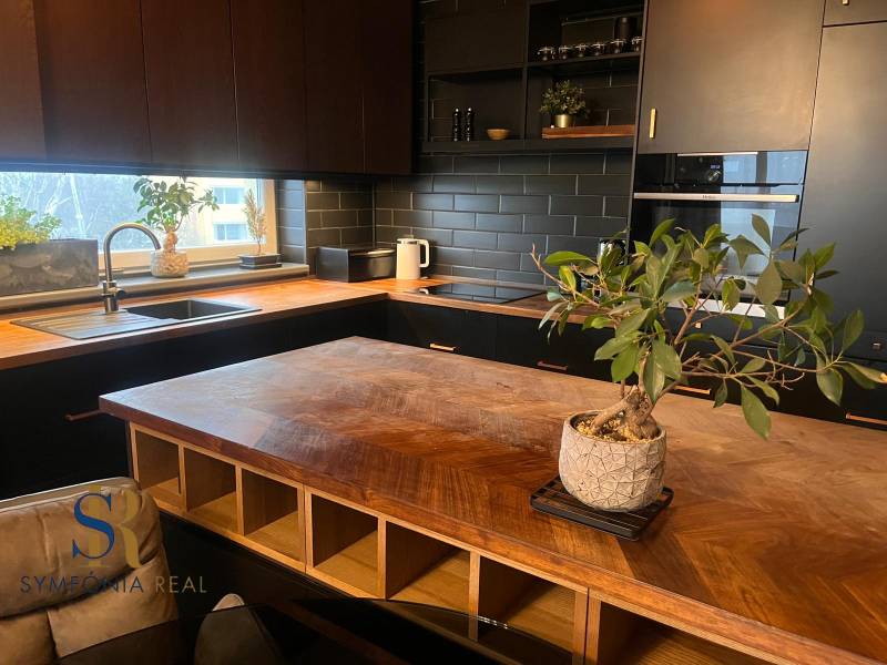 2-izbový byt v Pezinku s vlastným parkovaním - REZERVOVANÉ - Kuchyňa v 2-izbovom byte s podlahou s dreveným dekorom a čiernou kuchynskou linkou.