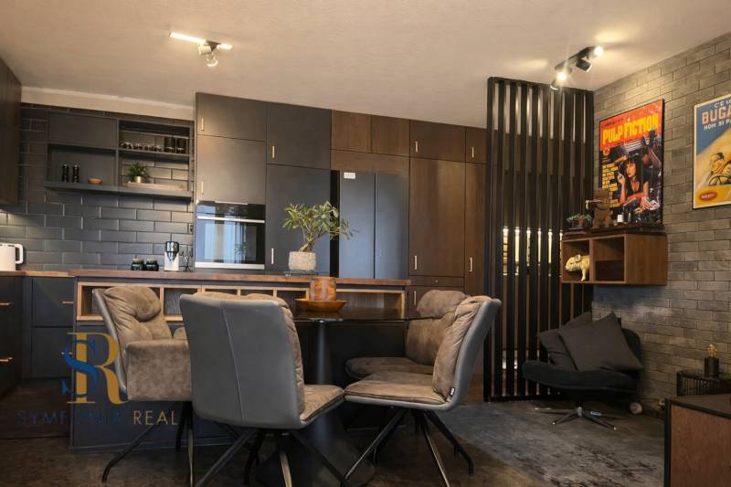 2-izbový byt v Pezinku s vlastným parkovaním - REZERVOVANÉ - Kuchyňa v 2-izbovom byte s tmavými skrinkami a dekoratívnymi plagátmi na stene.