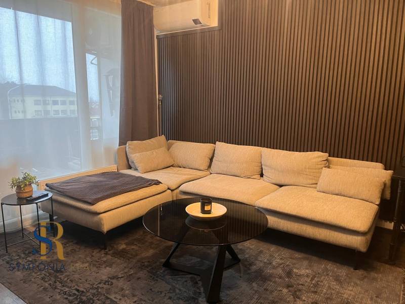 2-izbový byt v Pezinku s vlastným parkovaním - REZERVOVANÉ - Svetlá pohovka v 2-izbovom byte s dreveným dekórom na stene a stolíkom.