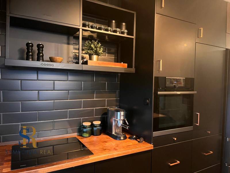 2-izbový byt v Pezinku s vlastným parkovaním - REZERVOVANÉ - Kuchyňa s čiernymi skrinkami v 2-izbovom byte a podlahou s dreveným dekorom.