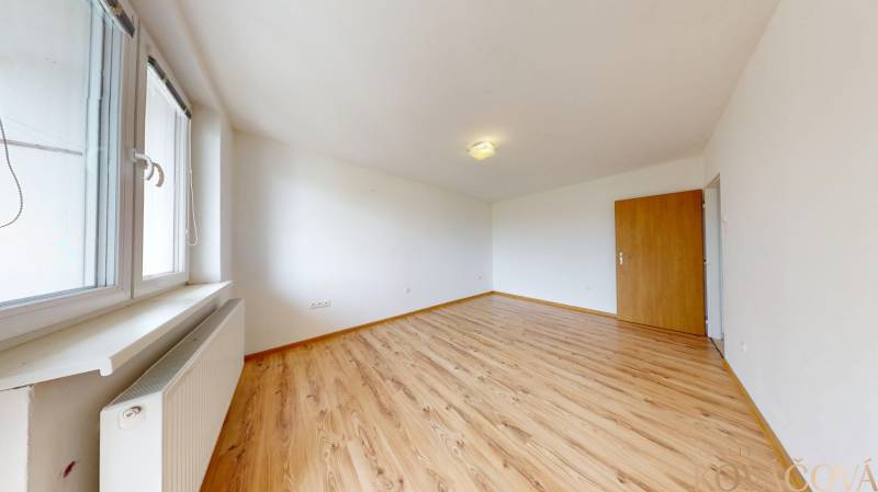 Na prenájom 2 izbový byt, Dežerice - Izba s podlahou s dreveným dekorom v 2-izbovom byte a veľkým oknom.