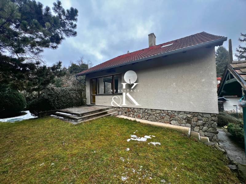 Predaj rekreačná chata s pozemkom, garážou a saunou Modra, Harmónia - Chata pri Modre s trávnatým pozemkom, kamennými schodmi a ihličnatými stromami.