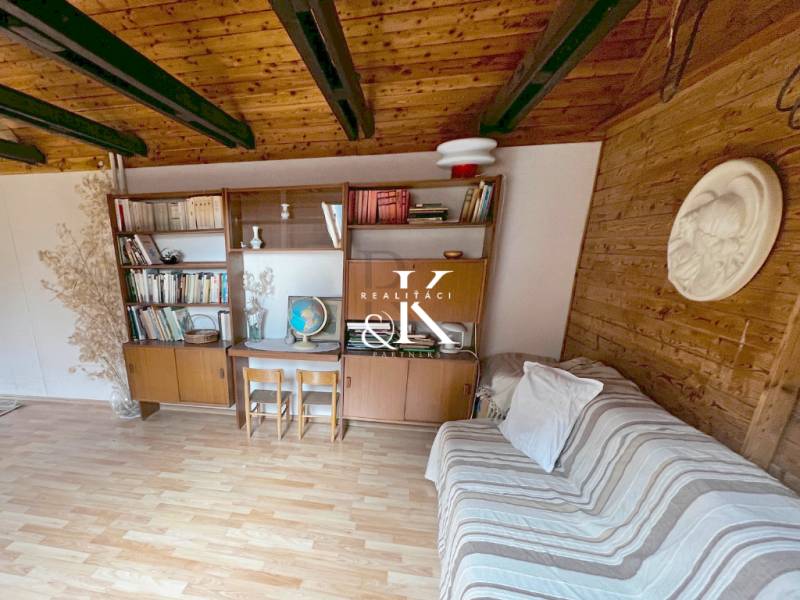 Predaj rekreačná chata s pozemkom, garážou a saunou Modra, Harmónia - Interiér chaty s drevenými trámami, nábytkom a podlahou s dreveným dekorom.