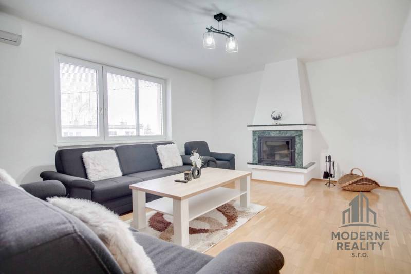 Na prenájom veľký 4-izbový byt s balkónom, garážou a záhradou, Kolta – - Obývacia izba v 4-izbovom byte s krbom a podlahou s dreveným dekorom.