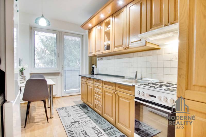 Na prenájom veľký 4-izbový byt s balkónom, garážou a záhradou, Kolta – - Kuchyňa v 4-izbovom byte s podlahou s dreveným dekorom a jedálenským stolom.