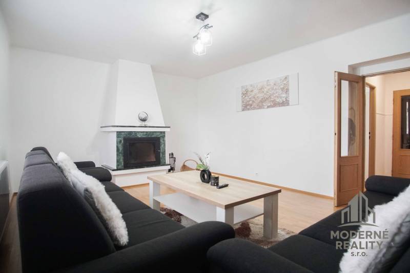 Na prenájom veľký 4-izbový byt s balkónom, garážou a záhradou, Kolta – - Obývacia izba v 4-izbovom byte s krbom a podlahou s dreveným dekorom.