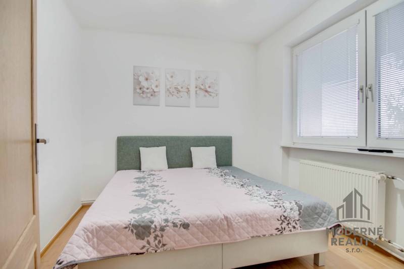 Na prenájom veľký 4-izbový byt s balkónom, garážou a záhradou, Kolta – - Spálňa so svetlou posteľou, podlahou s dreveným dekorom a ozdobnými obrazmi v 4-izbovom byte.