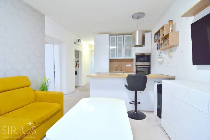 ŠTÚROVA, 3-i byt, 75 m2 – komplet rekonštrukcia, vlastné parkovanie - Kuchyňa a obývačka v 3-izbovom byte s bielym nábytkom a žltou sedačkou.