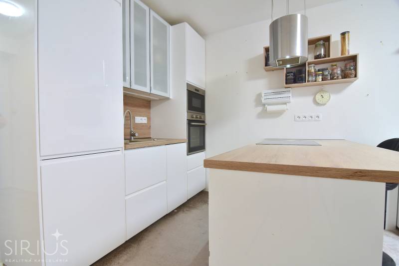 ŠTÚROVA, 3-i byt, 75 m2 – komplet rekonštrukcia, vlastné parkovanie - Kuchyňa v 3-izbovom byte s bielymi skrinkami a dreveným dekorom pracovnej dosky.