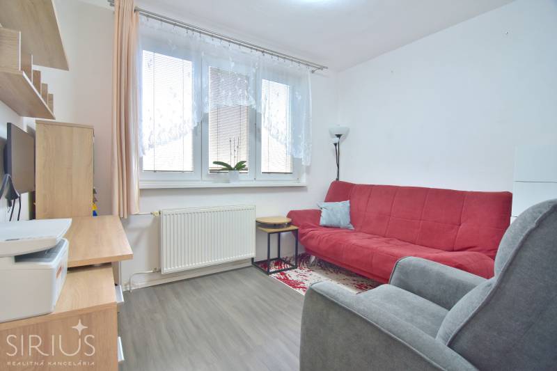 ŠTÚROVA, 3-i byt, 75 m2 – komplet rekonštrukcia, vlastné parkovanie - Izba v 3-izbovom byte s červenou sedačkou, kancelárskym stolom a podlahou s dreveným dekorom.