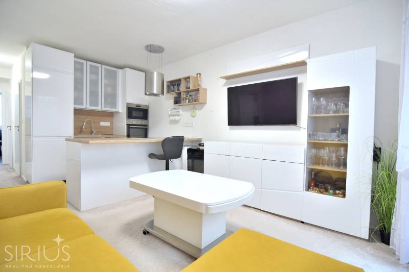 ŠTÚROVA, 3-i byt, 75 m2 – komplet rekonštrukcia, vlastné parkovanie - Obývacia izba s kuchyňou v 3-izbovom byte, biela nábytok, žltá sedačka, televízor.