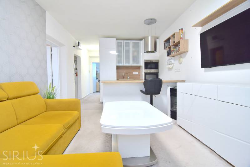 ŠTÚROVA, 3-i byt, 75 m2 – komplet rekonštrukcia, vlastné parkovanie - Obývacia izba v 3-izbovom byte s kuchyňou, žltou sedačkou a televízorom na stene.