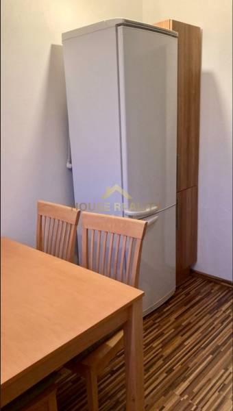 Prenájom 3 izbový byt, ulica Jána Poničana, BA IV. Devínska Nová Ves - Kuchyňa v 3-izbovom byte s chladničkou, drevený stôl a stoličky, podlaha s dreveným dekorom.