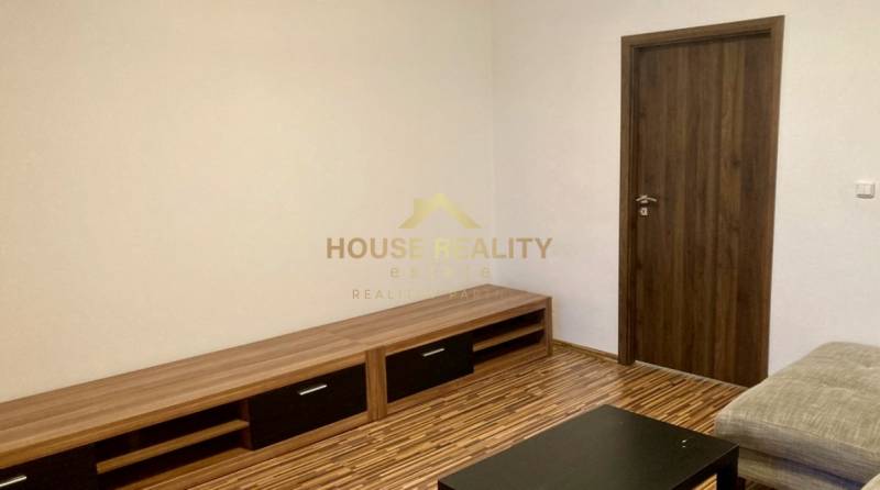 Prenájom 3 izbový byt, ulica Jána Poničana, BA IV. Devínska Nová Ves - Obývacia izba s podlahou s dreveným dekorom v 3-izbovom byte, svetlé steny, drevený nábytok.