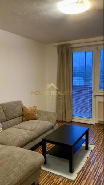 Prenájom 3 izbový byt, ulica Jána Poničana, BA IV. Devínska Nová Ves - Obývacia izba s pohovkou, čiernym stolíkom a podlahou s dreveným dekorom v 3-izbovom byte.