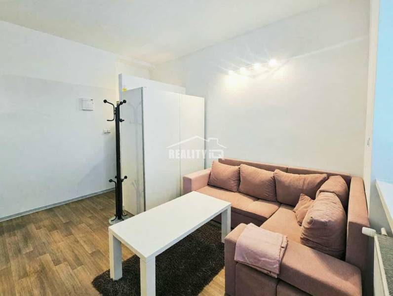 Prenájom, Garsónka, M.R.Štefánika, Centrum, Žilina - Garsónka s rohovou sedačkou, bielym stolíkom a podlahou s dreveným dekorom.